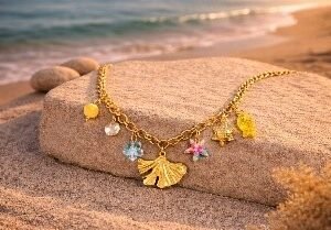 Gold mermaid tail charm necklace with crystal and flower charms on beach by Lumera